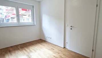Helles, unmöbliertes Zimmer mit Parkettboden und weiß gestrichenen Wänden, bereit zur Einrichtung.