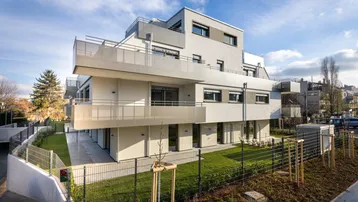 Modernes Mehrfamilienhaus mit klaren Linien, großzügigen Balkonen und gepflegten Grünflächen.