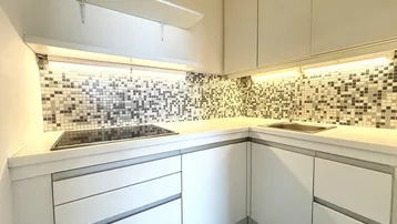 Moderne Einbauküche mit weißen Schränken, Mosaikfliesen und Induktionskochfeld, gut beleuchtet.