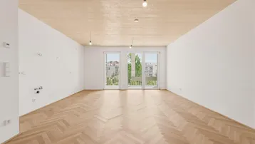Helles, leeres Zimmer mit Fischgrätparkett, Holzbalkendecke und Zugang zu einem französischen Balkon.