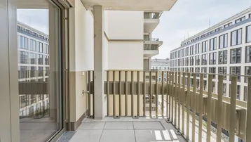 Moderner Balkon mit Fliesenboden und Blick auf umliegende Gebäude in urbaner Umgebung.