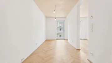 Helles Zimmer mit Fischgrätparkettboden und Holzbalkendecke, bietet Zugang zu einem Balkon.