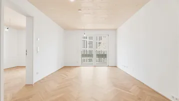 Helles, leeres Zimmer mit Fischgrätparkettboden und Zugang zu einem französischen Balkon.