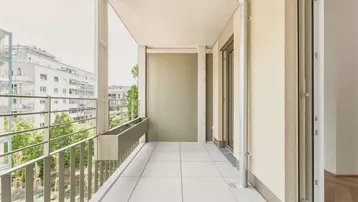 Heller Balkon mit Fliesenboden und Blick auf die umliegenden Gebäude und Grünflächen.