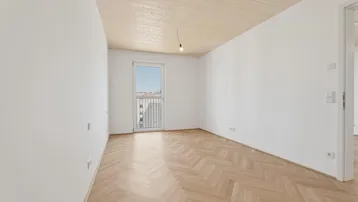 Helles, leeres Zimmer mit Fischgrätparkettboden und Zugang zu einem französischen Balkon.