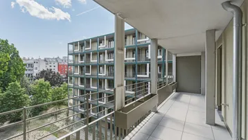 Langer, schmaler Balkon mit Fliesenboden und Blick auf die umliegenden Gebäude und Bäume.