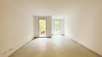 Helles, leeres Zimmer mit Fliesenboden und Zugang zu einem französischen Balkon, ideal als Wohnbereich.