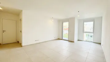 Helles und geräumiges Wohnzimmer mit großen Fliesen, weißen Wänden und Zugang zu einem Balkon.