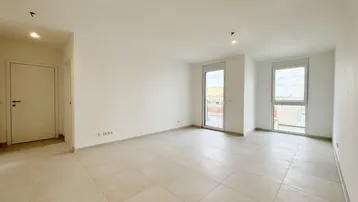 Helles, leeres Wohnzimmer mit großen Fenstern und Zugang zu einem möglichen Balkon.