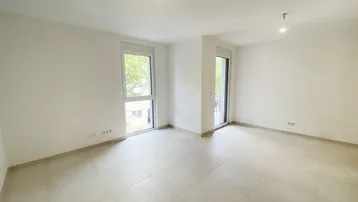 Helles, leeres Zimmer mit großen Fenstern und Fliesenboden, bereit zur individuellen Gestaltung.