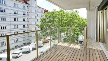 Moderner Balkon mit Holzfußboden und Glasgeländer, bietet Blick auf die Straße und umliegende Gebäude.