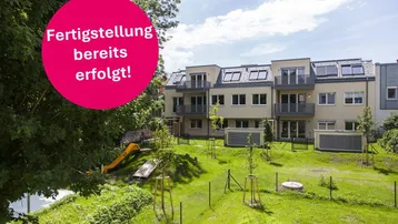 Modernes Mehrfamilienhaus mit Balkonen, gepflegtem Garten und Kinderspielplatz unter blauem Himmel.