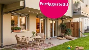 Gemütliche Terrasse mit Gartenanteil und Sitzgelegenheiten vor einem modernen Wohngebäude, ideal zum Entspannen.