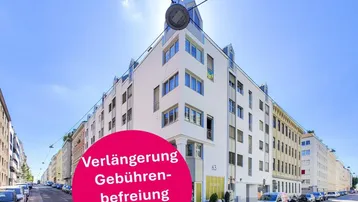 Modernes Mehrfamilienhaus an einer belebten Stadtstraße mit klarem Himmel und vielen Fenstern.