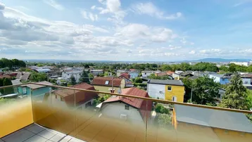 Geräumiger Balkon mit Glasbrüstung und weitem Blick über die Stadt und die grüne Umgebung.