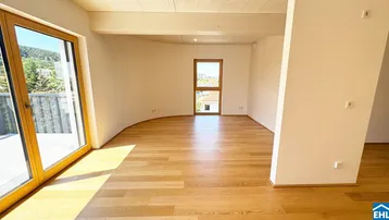 Helles, leeres Wohnzimmer mit Holzboden und Zugang zu einem Balkon, bietet viel natürliches Licht.