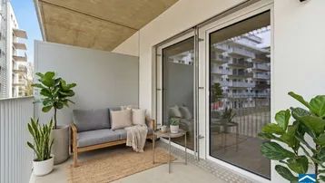 Moderner Balkon mit bequemen Sitzmöbeln und Pflanzen, bietet einen Blick auf die umliegenden Gebäude.