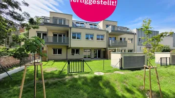 Modernes Mehrfamilienhaus mit Balkonen und großzügiger Grünfläche im Vordergrund, kürzlich fertiggestellt.
