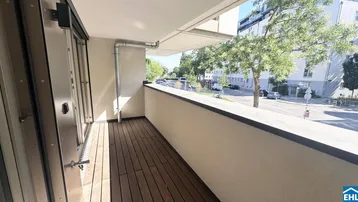 Heller Balkon mit Holzboden und Blick auf die Straße sowie umliegende Gebäude.
