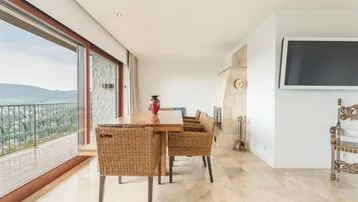 Essbereich mit Holztisch, Korbstühlen, Marmorboden und Zugang zu einem Balkon mit Aussicht.