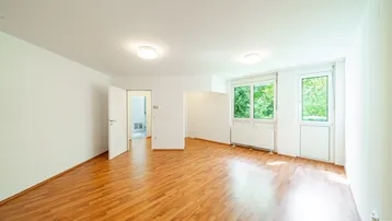 Helles Zimmer mit Laminatboden und weißen Wänden, bereit zur individuellen Gestaltung.