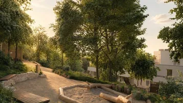 Sonniger Außenbereich mit naturnahem Spielplatz, umgeben von Bäumen und modernen Wohngebäuden im Hintergrund.