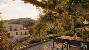 Sonnige Terrasse unter einer bewachsenen Pergola mit modernen Gartenmöbeln und weitem Blick auf die grüne Hügellandschaft.