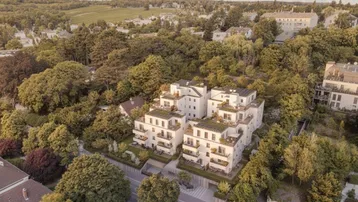 Moderne Wohnanlage mit weißer Fassade, Balkonen und Terrassen, umgeben von viel Grün und mit Fernblick.