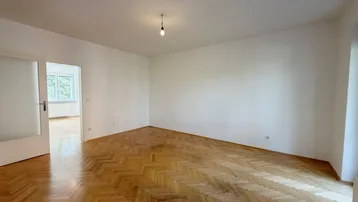 Helles Zimmer mit klassischem Fischgrätparkett und weißen Wänden, bereit zur individuellen Gestaltung.