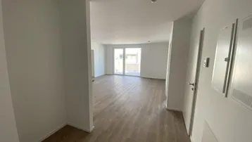 Heller Flur mit Laminatboden, der zu einem lichtdurchfluteten Wohnbereich mit Balkonzugang führt.