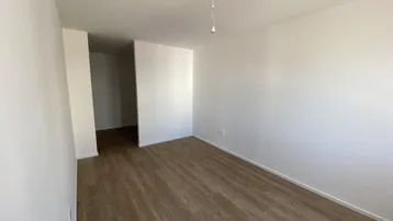 Helles, leeres Zimmer mit modernem Laminatboden und weißen Wänden, bereit zur individuellen Gestaltung.