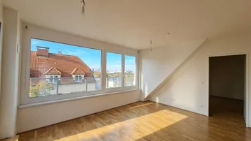Heller Wohnraum mit Holzboden, großen Fenstern und Blick über die Dächer der Stadt.