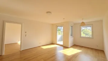 Helles Wohnzimmer mit Parkettboden und Zugang zum Balkon, durchflutet von natürlichem Sonnenlicht.
