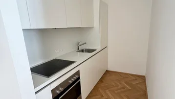 Moderne, kompakte Küchenzeile mit weißen Schränken, Kochfeld und Backofen in einem hellen Raum.