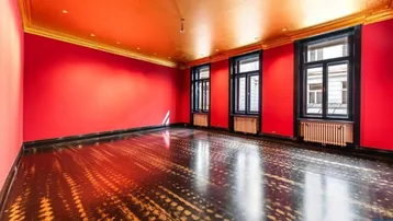 Geräumiger Raum mit leuchtend roten Wänden, goldener Decke und dunklem Fischgrätparkett.