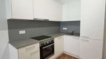 Moderne Einbauküche mit weißen Schränken, grauer Arbeitsplatte und integrierten Geräten.