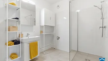 Modernes Badezimmer mit ebenerdiger Dusche, Waschbecken und praktischen Ablageregalen in hellen Farben.