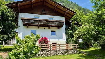 Traditionelles Haus mit Holzbalkonen und gepflegtem Garten in grüner Umgebung.