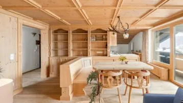 Gemütlicher Wohn-Essbereich im alpinen Stil mit Holztäfelung, Einbauschränken und Zugang zum Balkon.