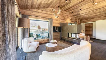 Gemütliches Wohnzimmer im alpinen Stil mit Kamin, Holzwänden und einem Fensterplatz mit Bergblick.
