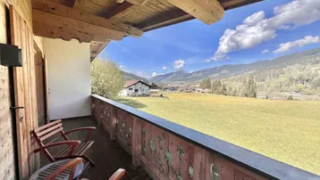Traditioneller Holzbalkon mit Sitzgelegenheiten und weitem Blick auf die Berge und grüne Wiesen.