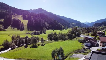 Weitläufiger Blick auf die grüne Berglandschaft mit Häusern und einem Bachlauf.