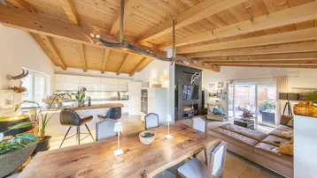 Geräumiger offener Wohn- und Essbereich mit Holzbalkendecke, moderner Küche und Zugang zur Terrasse.