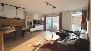 Helles, offenes Wohn-Esszimmer mit Holzboden, gemütlichem Sofa und Zugang zum Balkon.
