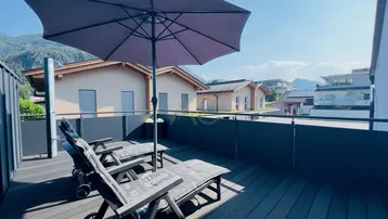 Sonniger Balkon mit Liegestühlen, Sonnenschirm und herrlichem Bergblick in die Natur.