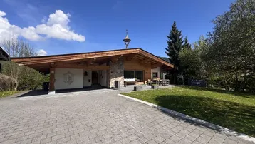 Charmantes Chalet mit Holzfassade, Carport und gepflasterter Auffahrt in ländlicher Umgebung.