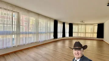 Geräumiges Wohnzimmer mit vielen Fenstern, hellem Laminatboden und weiß gestrichenen Wänden.