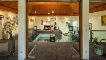 Geräumiger Eingangsbereich mit Glasflügeltüren, Teppichboden und einer modernen Skulptur.