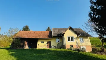 Gelbes Landhaus mit rotem Ziegeldach und angrenzendem Scheunengebäude auf einem grünen Hügel.