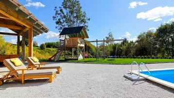 Großer Gartenbereich mit Swimmingpool, Kinderspielplatz und Liegestühlen unter einem Holzpavillon.